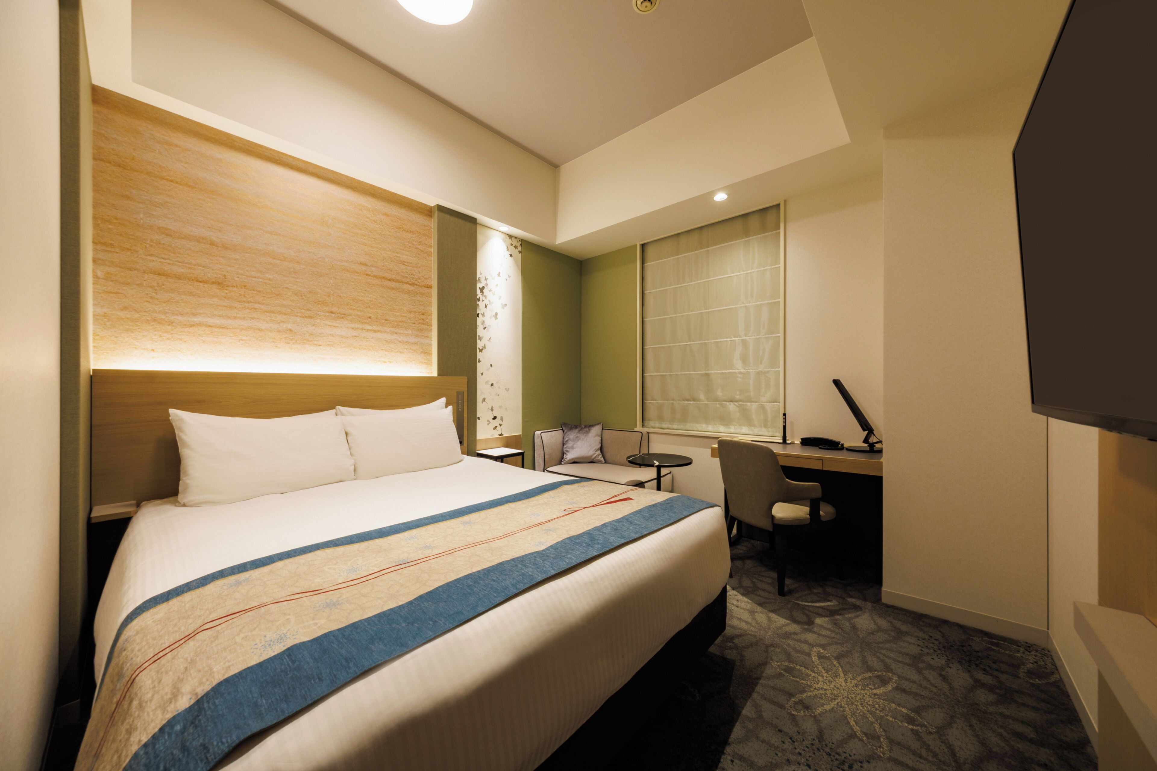 A hotel room with a large bed, a desk, a chair, and a window.