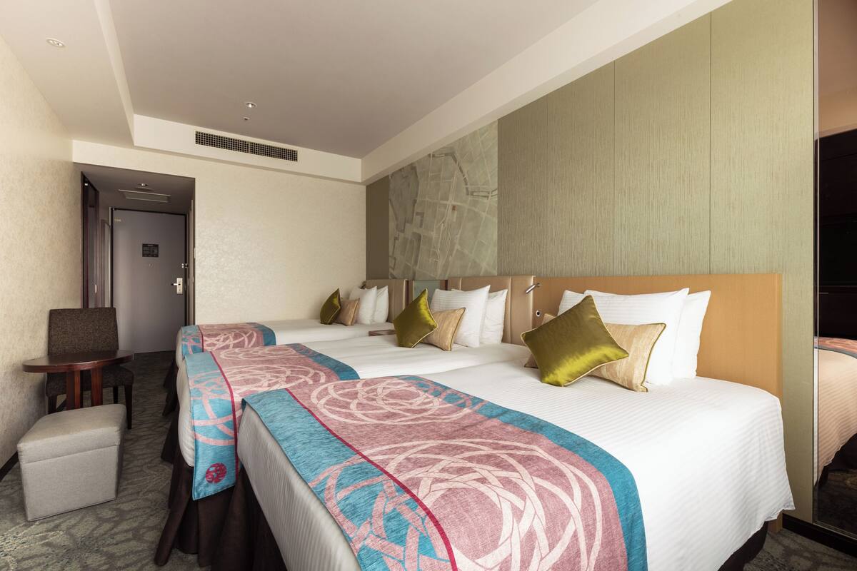 A hotel room with two beds, a small table, a chair, and a bench.