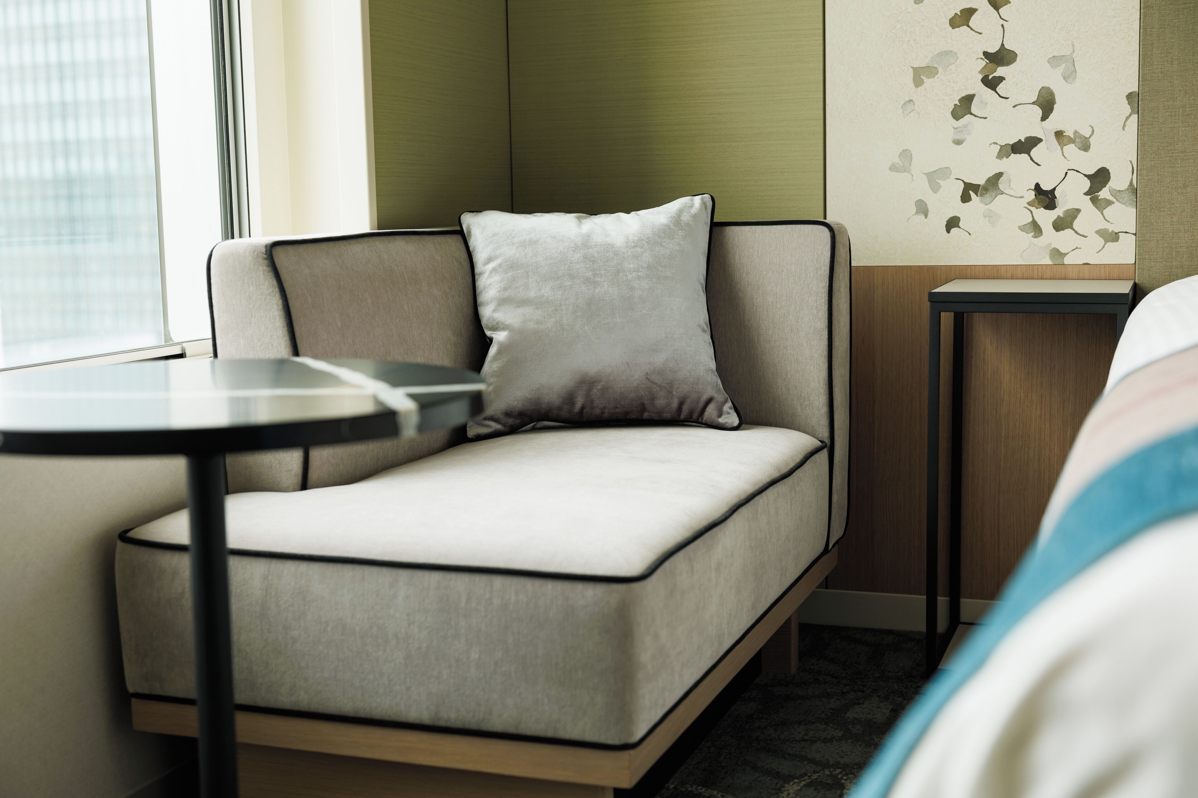 A modern hotel room with a sofa, a small table, and a wall with a leaf pattern.