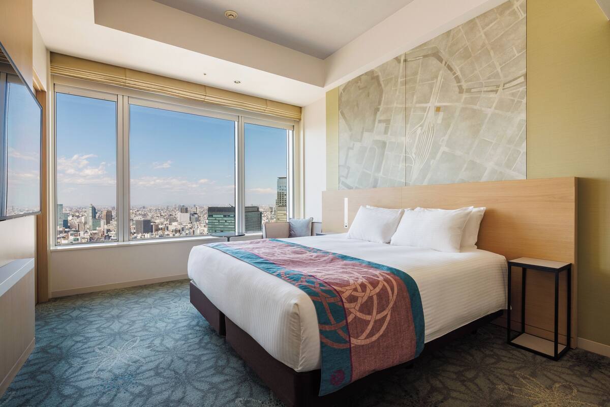 A hotel room with a large bed, a city view, and a map on the wall.