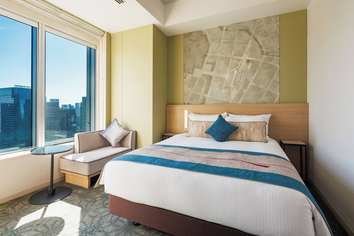 A hotel room with a large bed, a seating area, a city view, and a map on the wall.