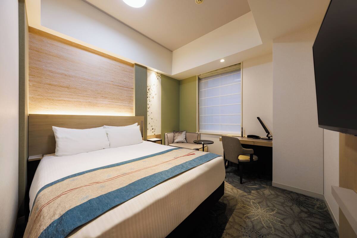 A hotel room with a large bed, a desk, a chair, and a TV.