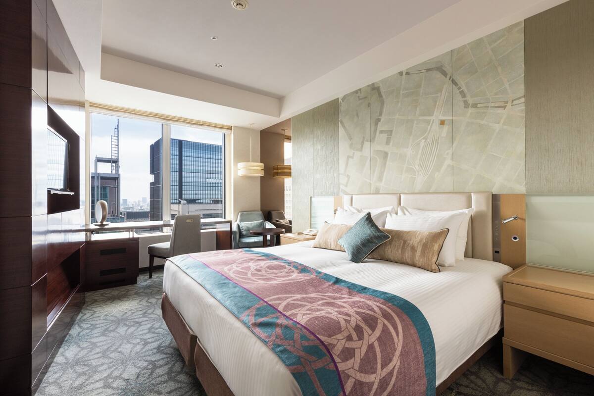 A hotel room with a large bed, a desk, and a view of the cityscape.