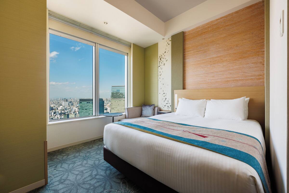 A hotel room with a large bed, a view of the city, and a cityscape through the window.