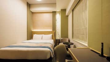A hotel room with a bed, a desk, a chair, and a window with blinds.