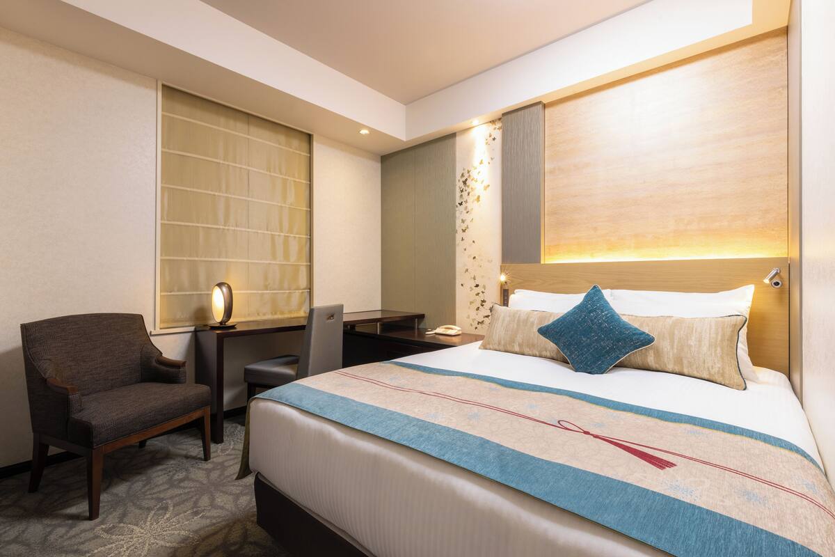 A hotel room with a large bed, a desk, a chair, and a nightstand.