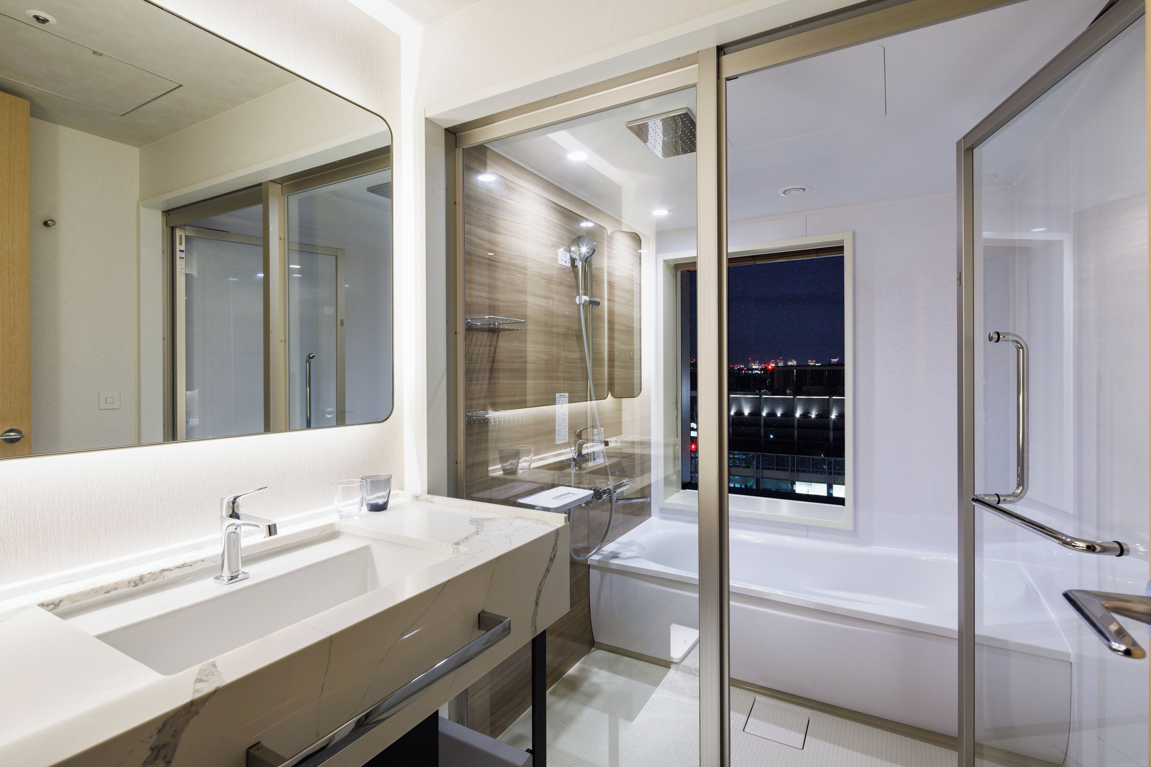 A modern bathroom with a large mirror, two sinks, a shower, and a bathtub.