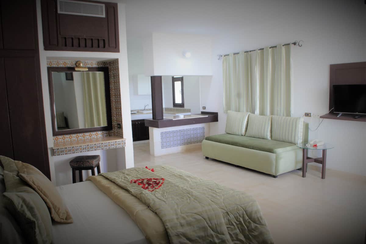 A hotel room with a bed, a sofa, a small table, a television, and a bathroom with a mirror and sink.