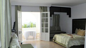 A hotel room with a bed, a sofa, a TV, and a balcony with a table and chairs.