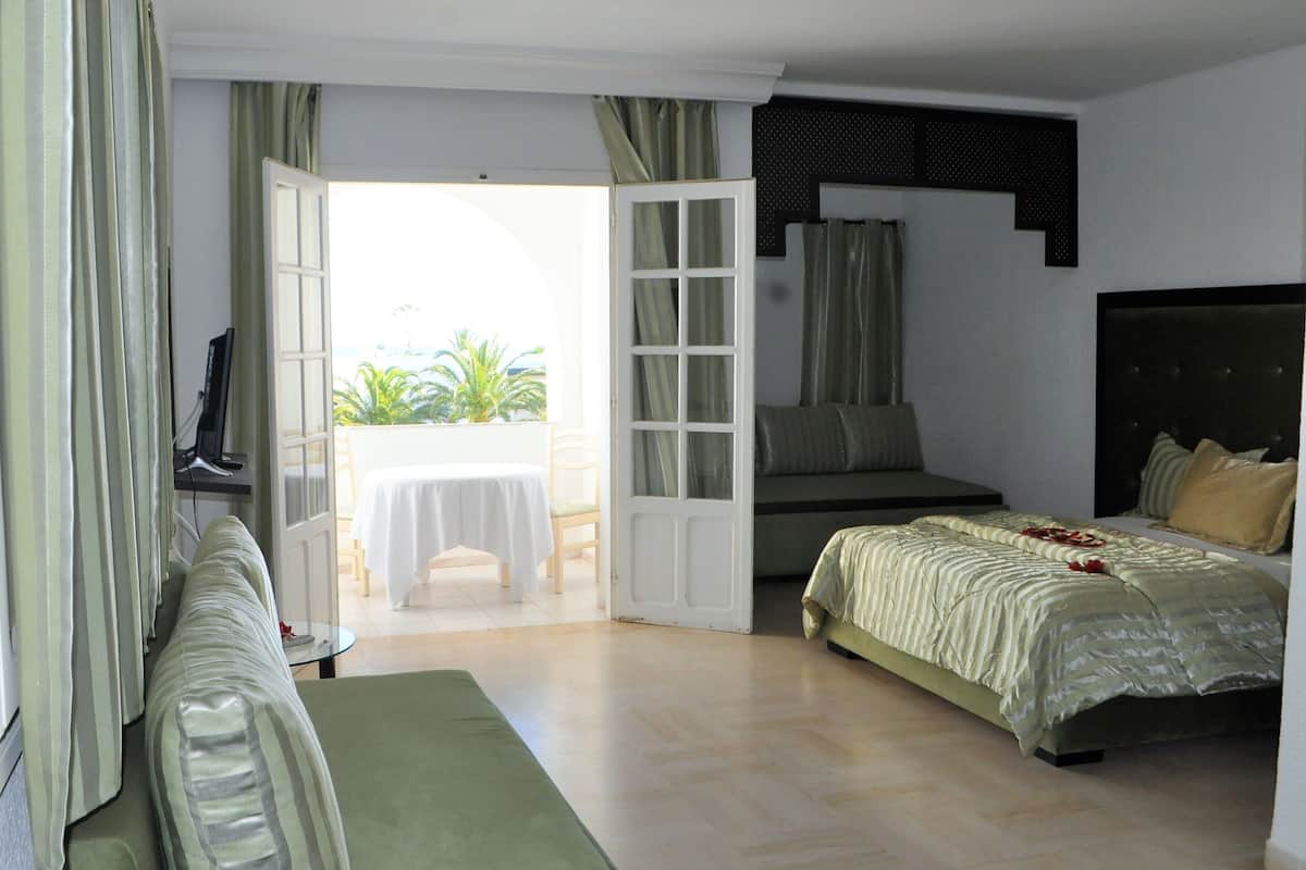A hotel room with a bed, a sofa, a TV, and a balcony with a table and chairs.