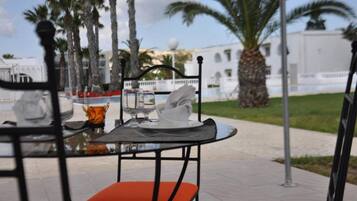 A table set outdoors with chairs, palm trees, and a building in the background.