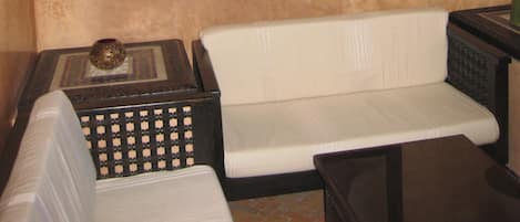 Una habitación con pared beige texturizada, una obra de arte enmarcada, un banco acolchado blanco, una mesita con un adorno y una lámpara.