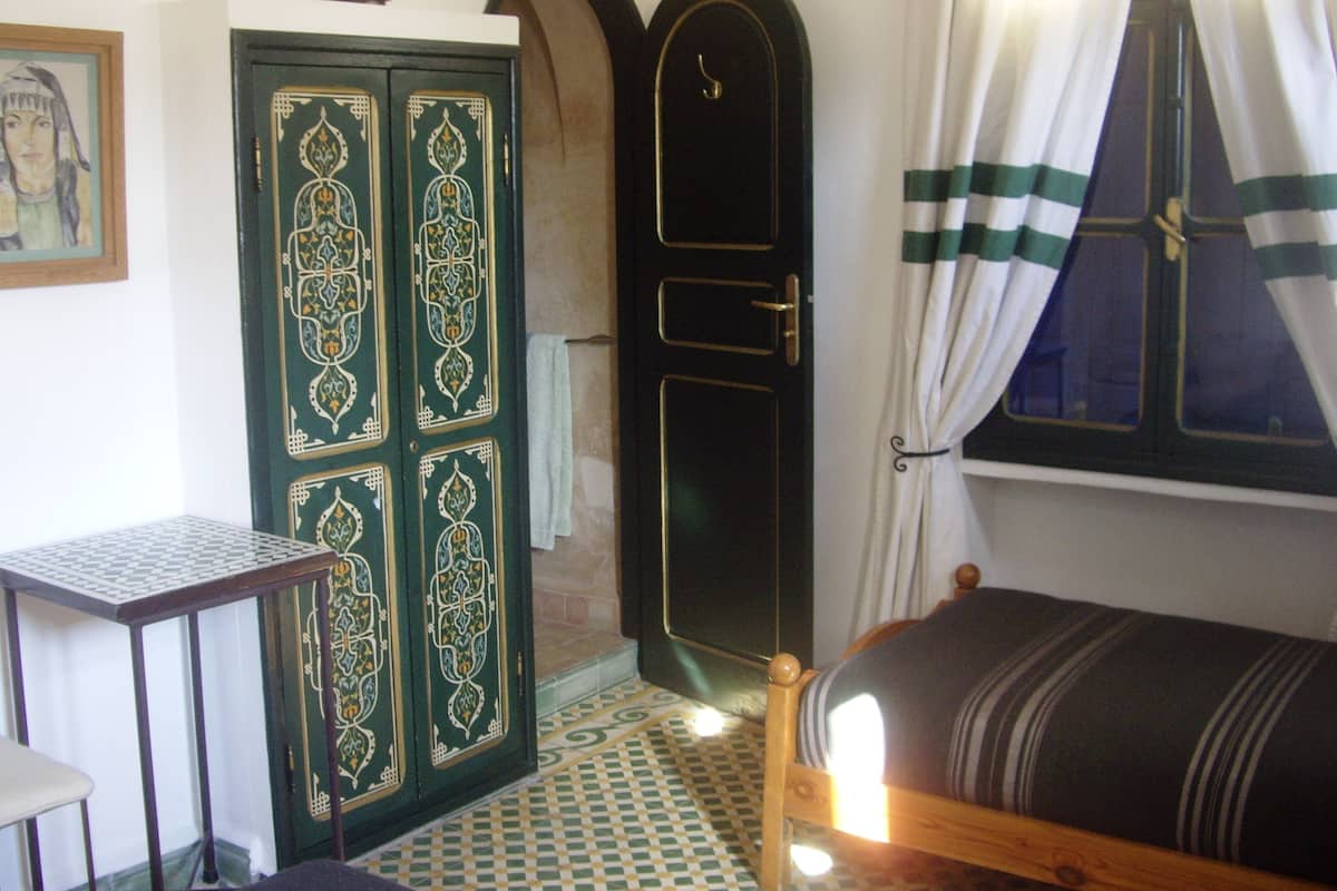 Una habitación con cama, escritorio, puerta de detalles elaborados y ventana con cortinas.