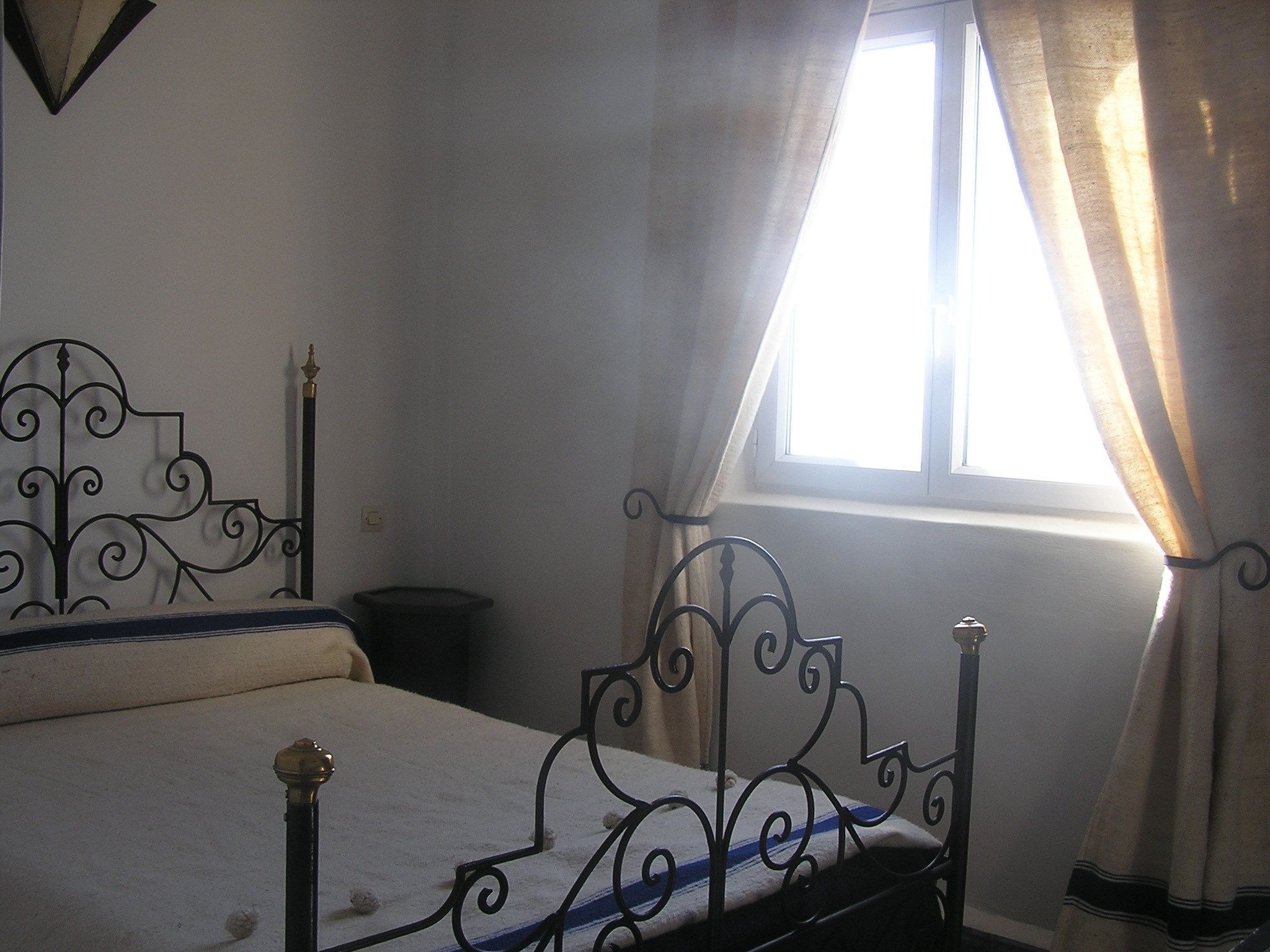 A bedroom with a bed, a window with curtains, and a wall-mounted light fixture.