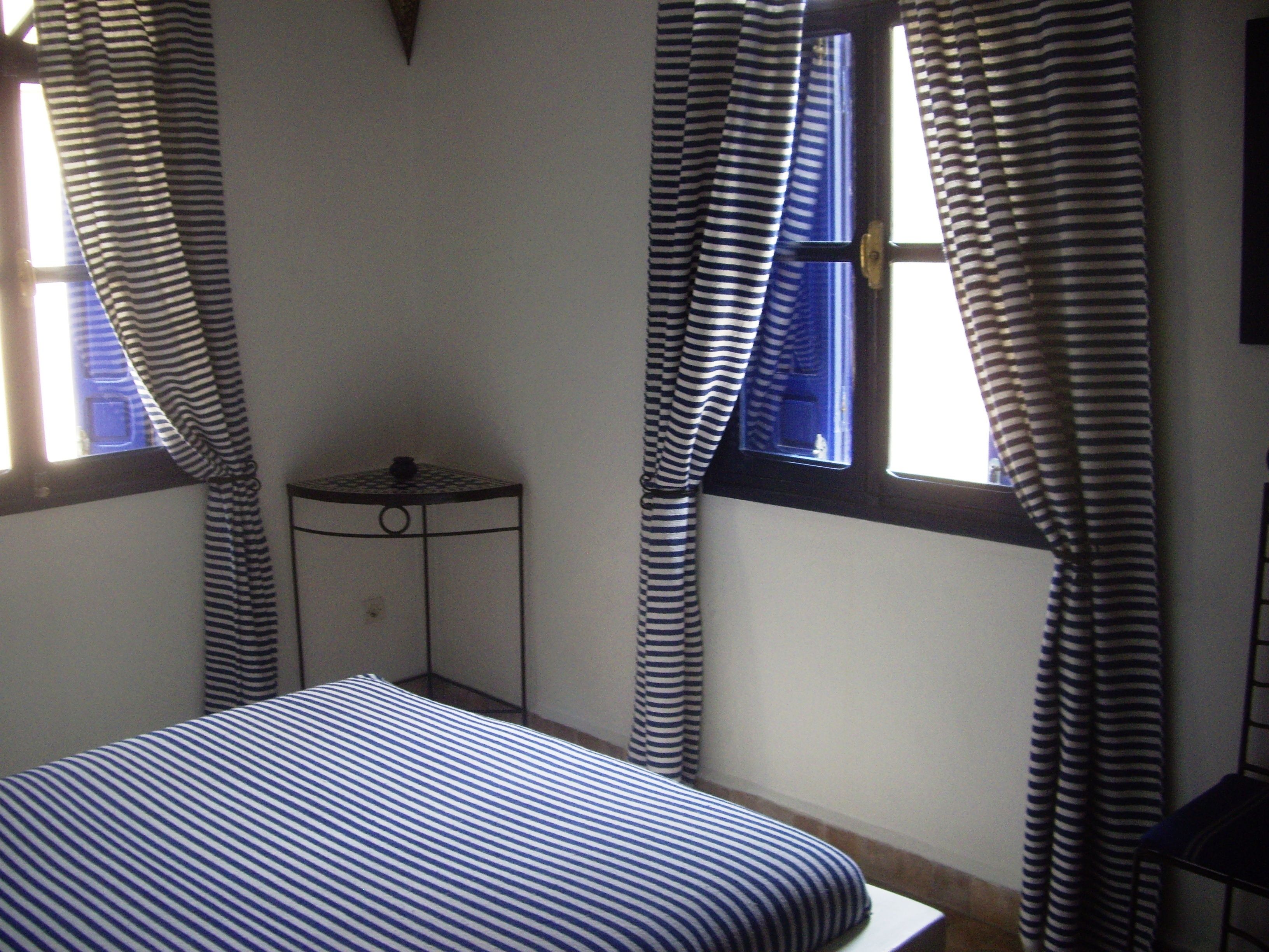 A bedroom with a bed, a small table, and curtains.