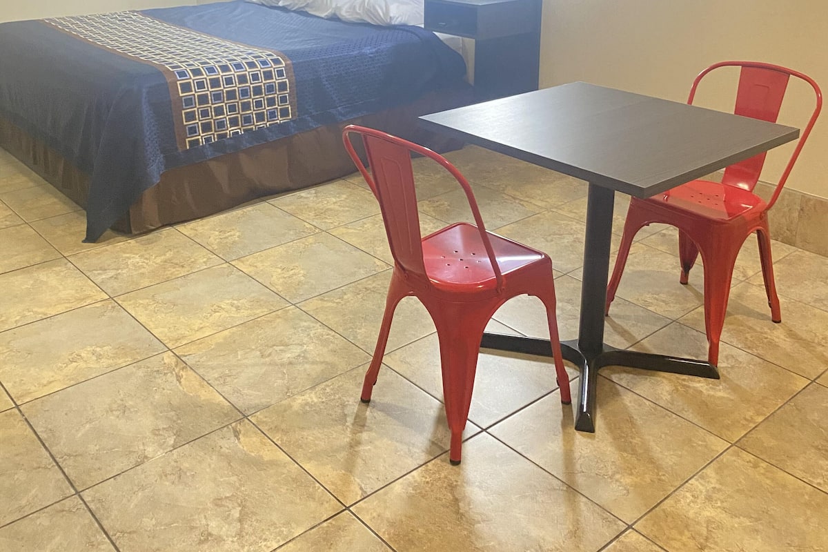 A room with a bed, a table, and two red chairs.
