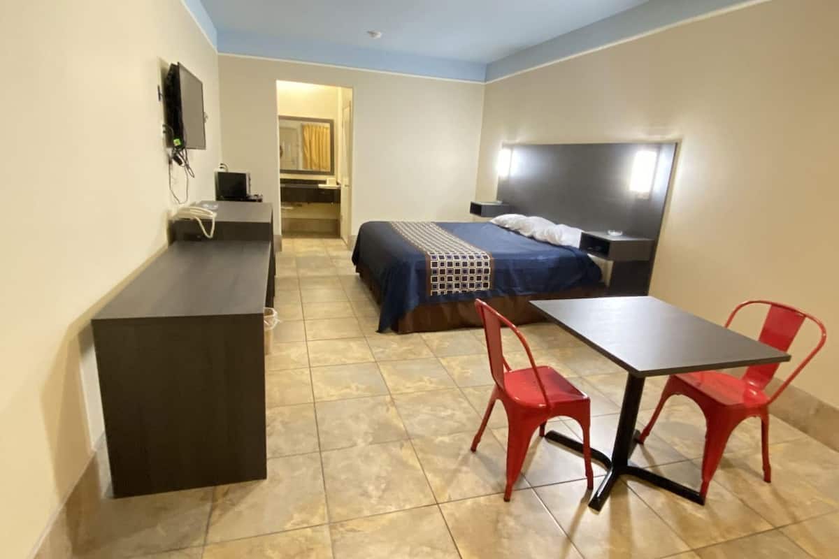 A compact hotel room with a bed, a desk, and two red chairs.