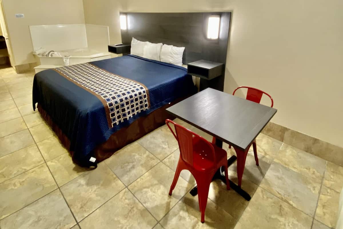 A hotel room with a bed, bedside table, and a small table with a chair.