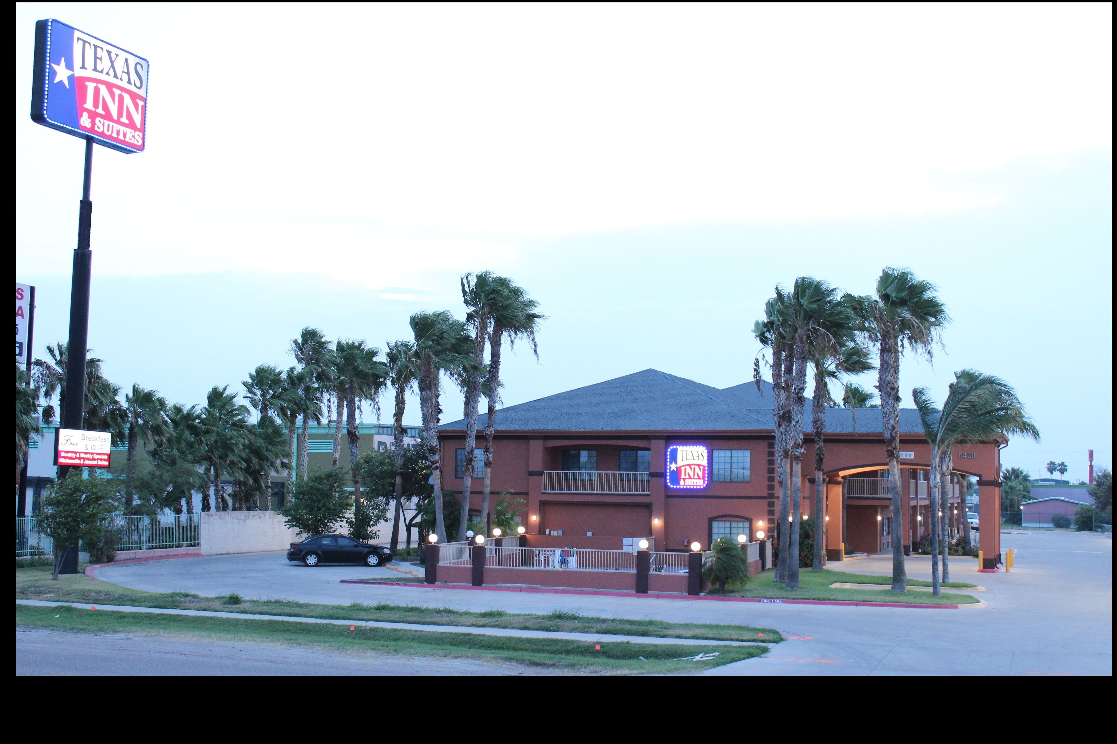 Edificio de Texas Inn & Suites con un letrero llamativo, rodeado de palmeras y un estacionamiento.