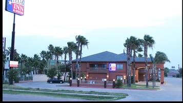Edificio de Texas Inn & Suites con un letrero llamativo, rodeado de palmeras y un estacionamiento.
