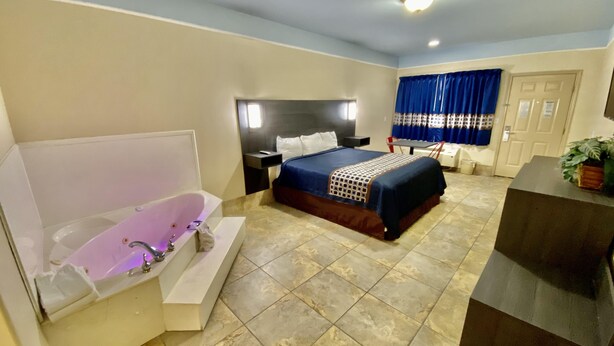 A modern hotel room with a large bed, a separate bathroom with a bathtub, a desk, and a potted plant.