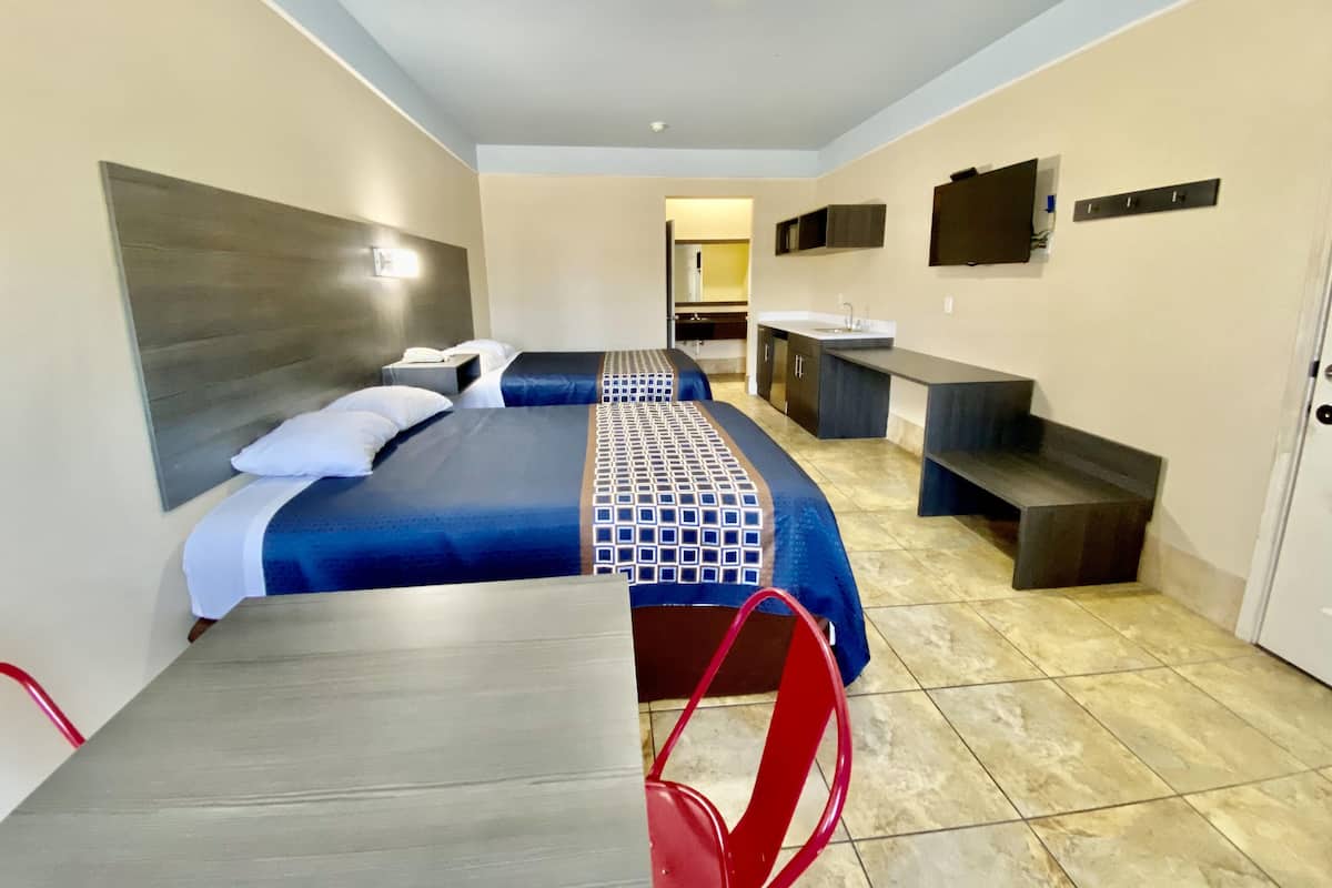 A hotel room with a bed, a desk, a chair, a sink, and a mirror.