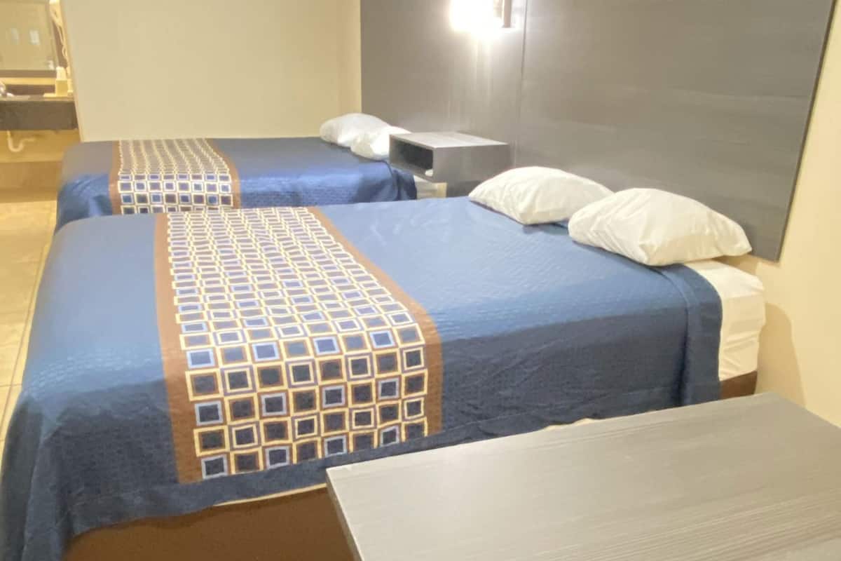 A hotel room with two beds, a nightstand, a desk, and a red chair.