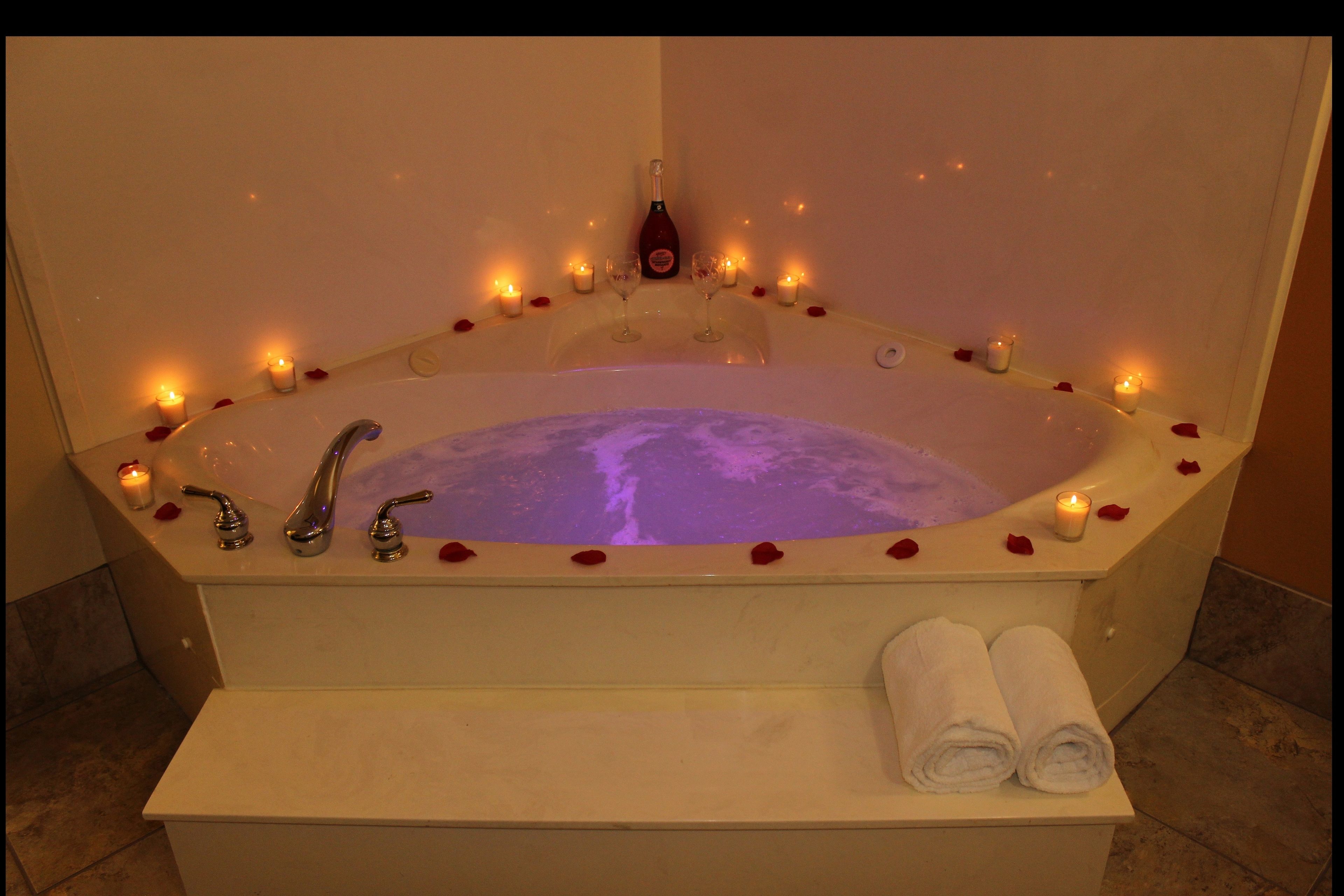A bathtub with rose petals and candles, a bottle of champagne, and towels.