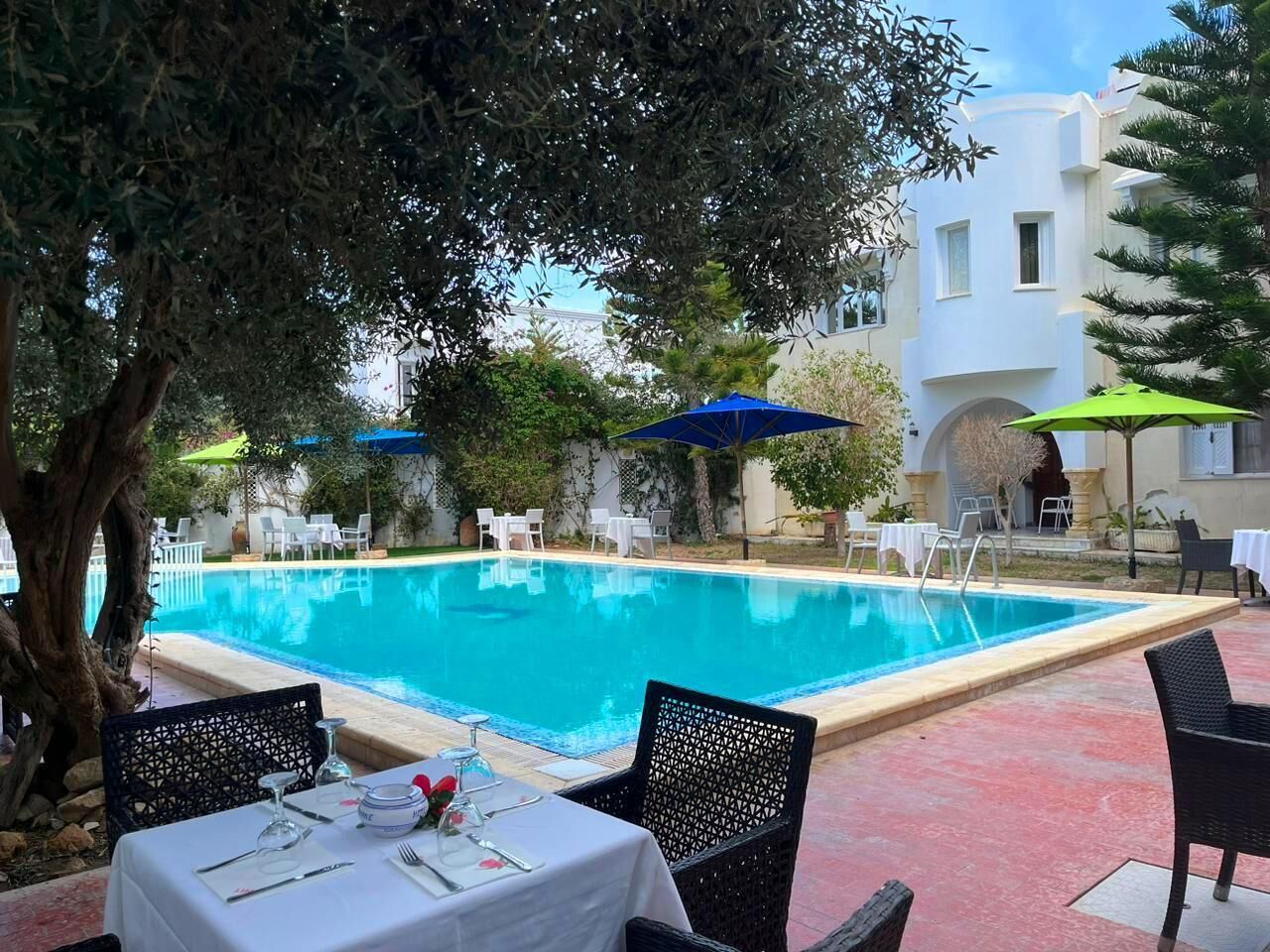 Un espace aménagé au bord de la piscine, avec une table à manger pour deux personnes, entourée de chaises et doté de parasols pour créer de l’ombre.