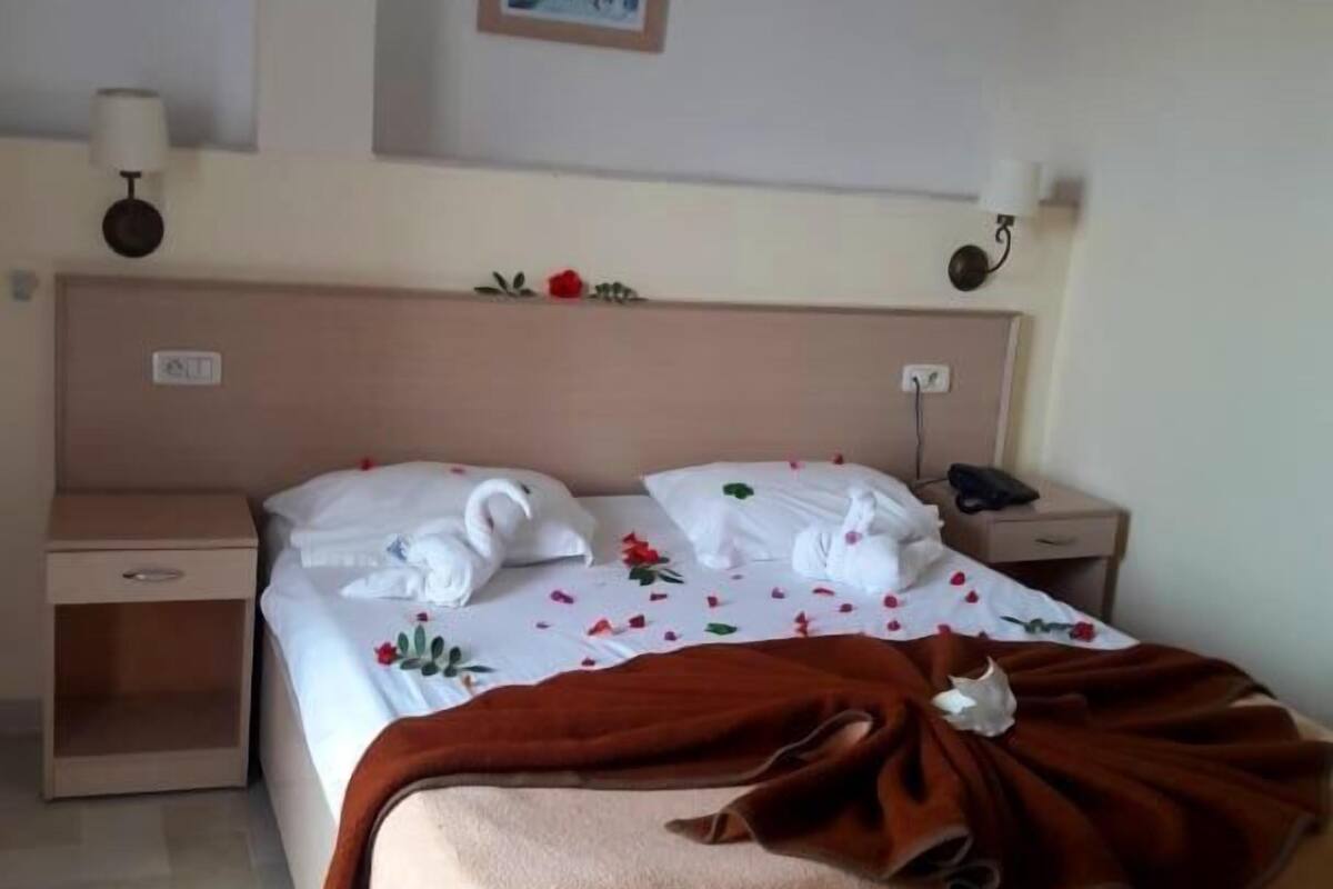 A hotel room with a bed, a nightstand, a wall-mounted lamp, and a framed picture above the bed.