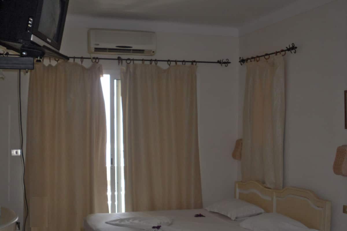 A hotel room with two beds, a television, an air conditioner, and a desk.