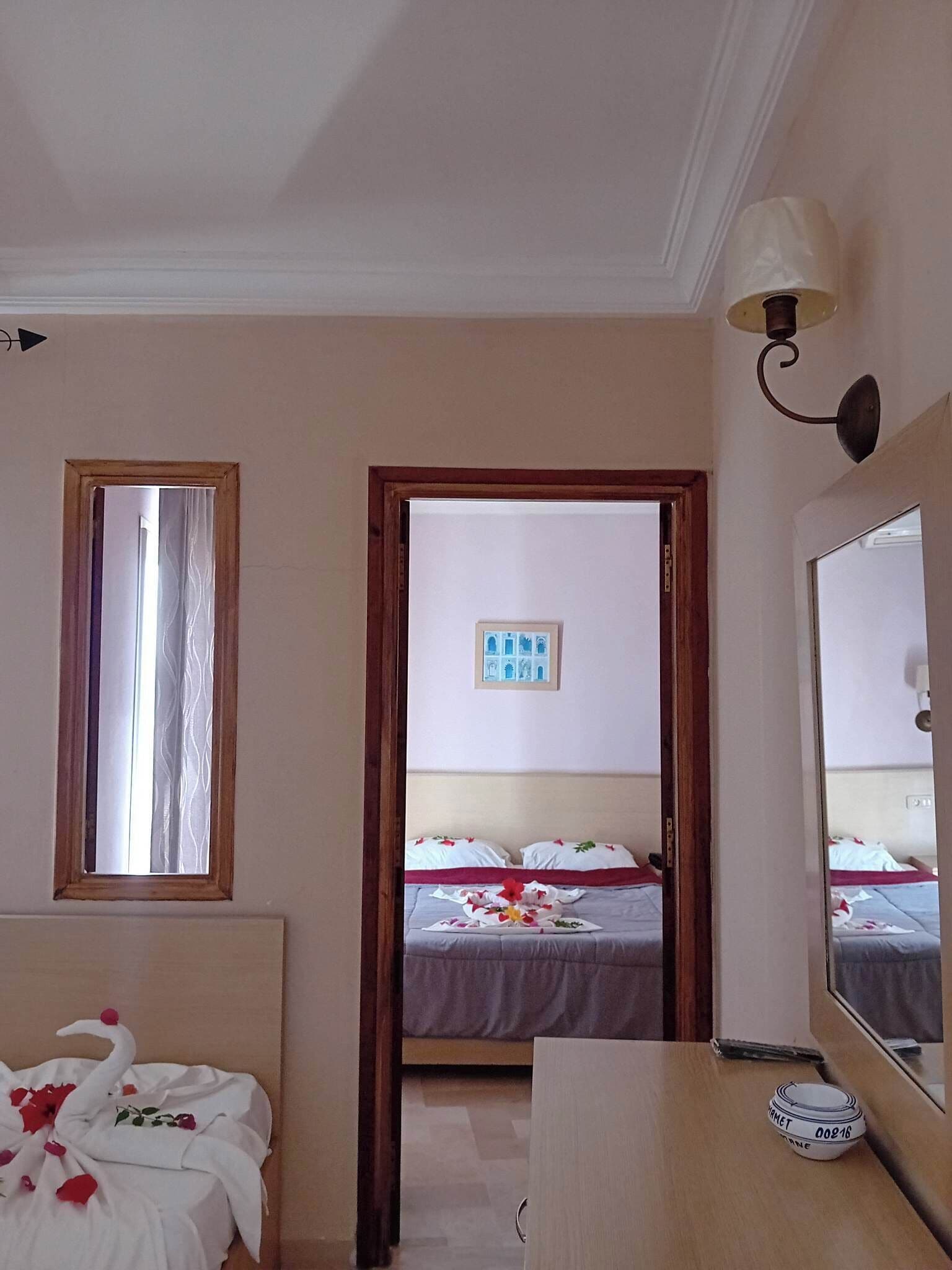 Habitación de hotel con cama, escritorio, espejo, un cuadro en la pared y ventana con cortinas.