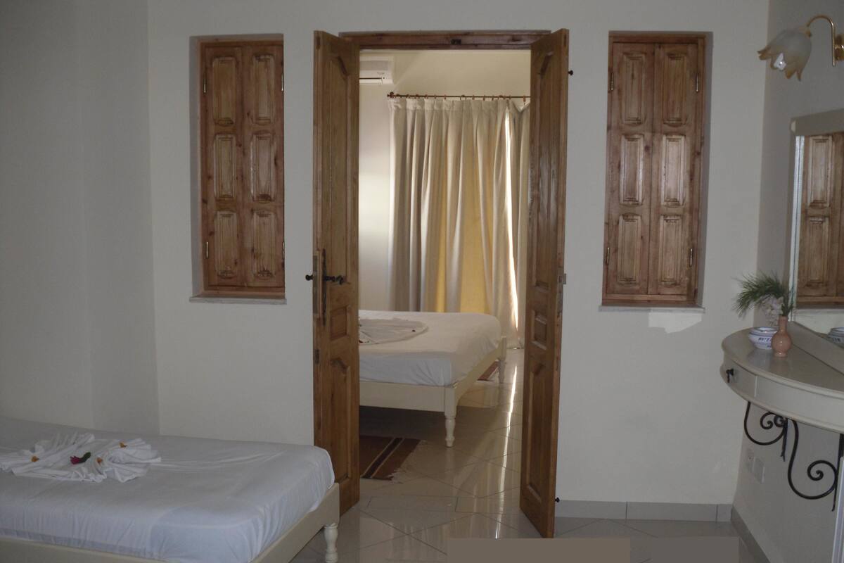A bedroom with a bed, a bathroom with a mirror, and a door leading to another room.