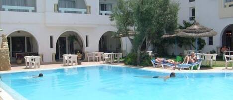 A swimming pool with lounge chairs and a thatched umbrella.