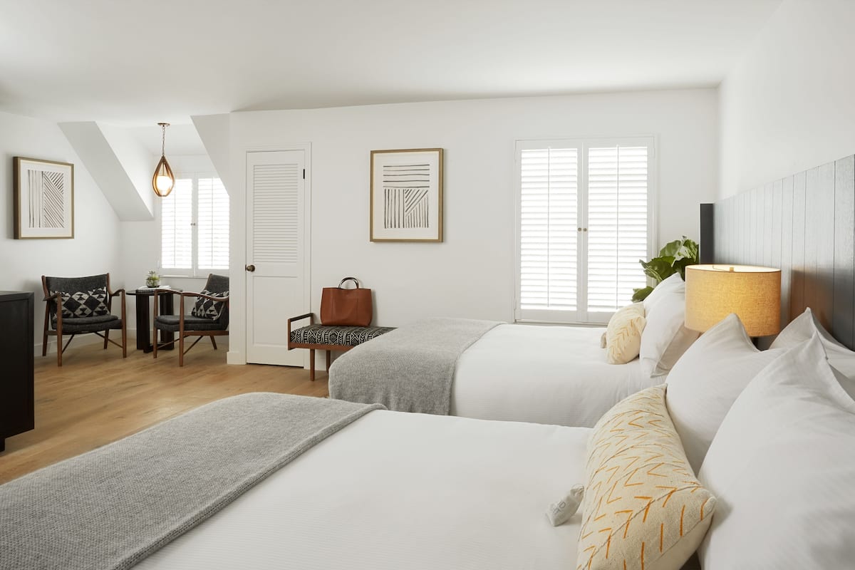 A hotel room with two beds, a desk, a chair, a lamp, and artwork on the walls.