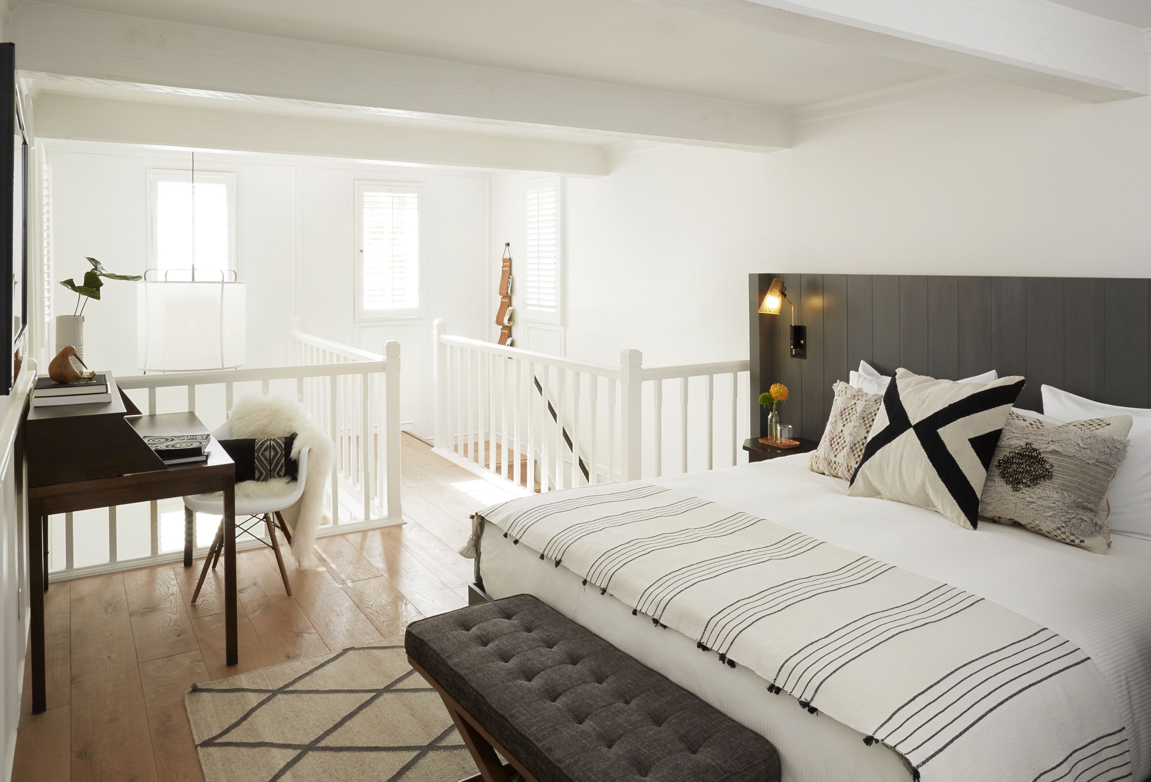 A bedroom with a large bed, a desk, and a chair. There is a balcony with a railing and a view of the outside.