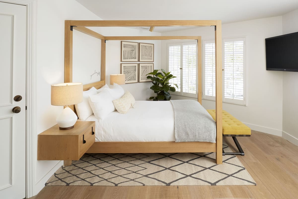 A bedroom with a four-poster bed, bedside tables, a TV, and a potted plant.