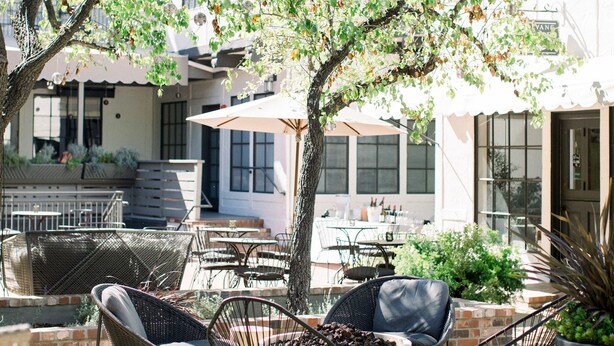 An outdoor seating area with wicker chairs, a round table, and a potted plant. - The Landsby (Solvang)