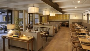 A restaurant with wooden tables, cushioned seating, pendant lighting, and a patterned wall. - The Landsby (Solvang)