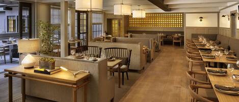 Un restaurant avec des tables en bois, des sièges rembourrés, des luminaires suspendus et un mur décoré de motifs.