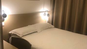 Una habitación de hotel con una cama, un escritorio y una mesita de noche. Hay lámparas de pared y un cuadro sobre la cama.