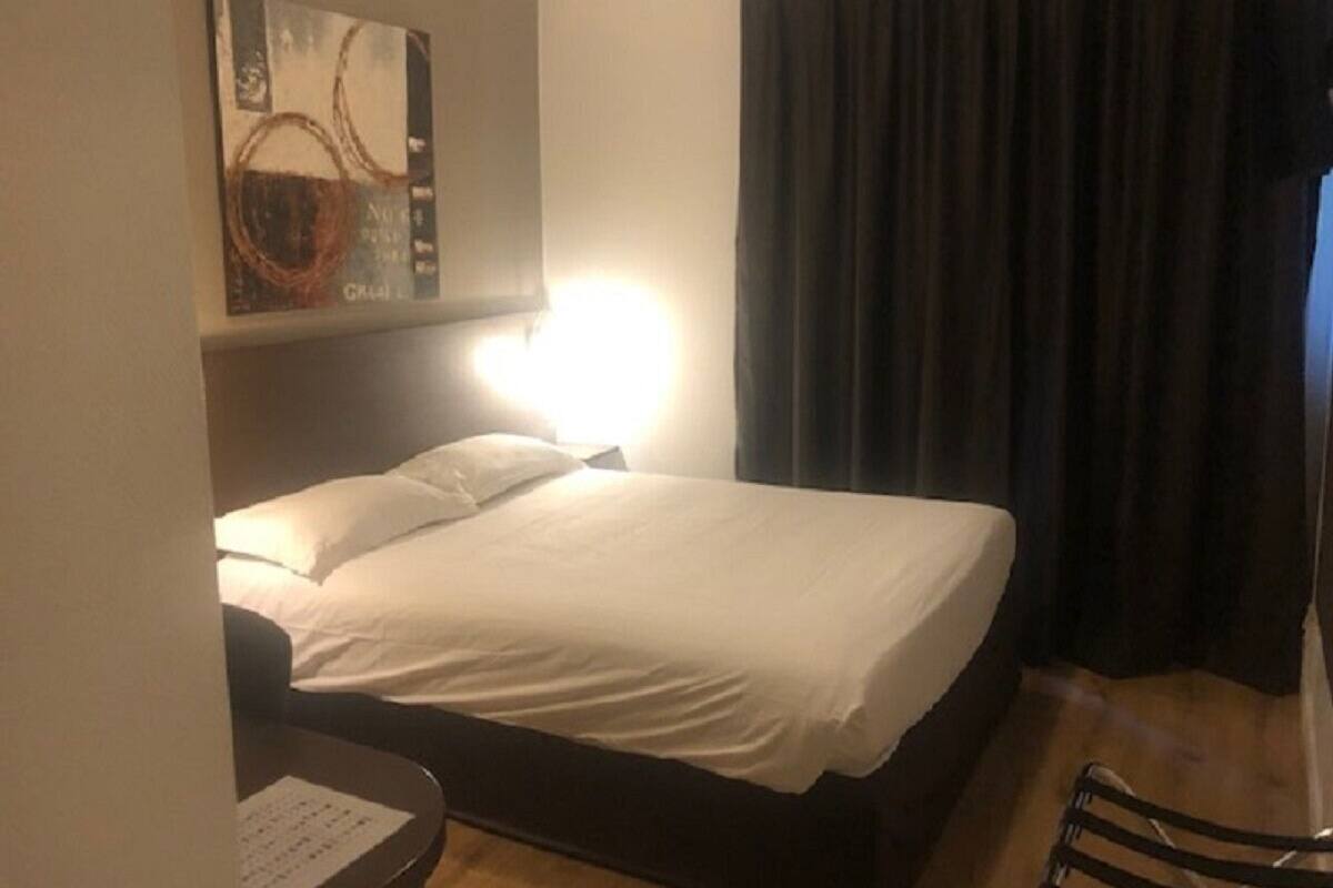 A hotel room with a bed, a desk, a chair, a wall-mounted artwork, and a window with curtains.