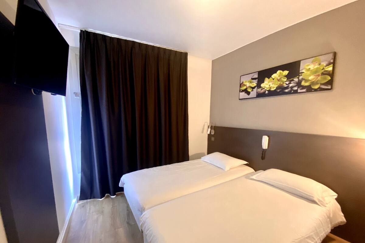 A hotel room with two beds, a flat-screen TV mounted on the wall, and a painting of orchids above the beds.