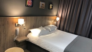 Habitación de hotel con cabecera de madera, cama con sábanas blancas, dos lámparas de noche, un teléfono y una mesita redonda.