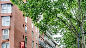Un hotel con un letrero rojo, varios pisos y un árbol en primer plano.
