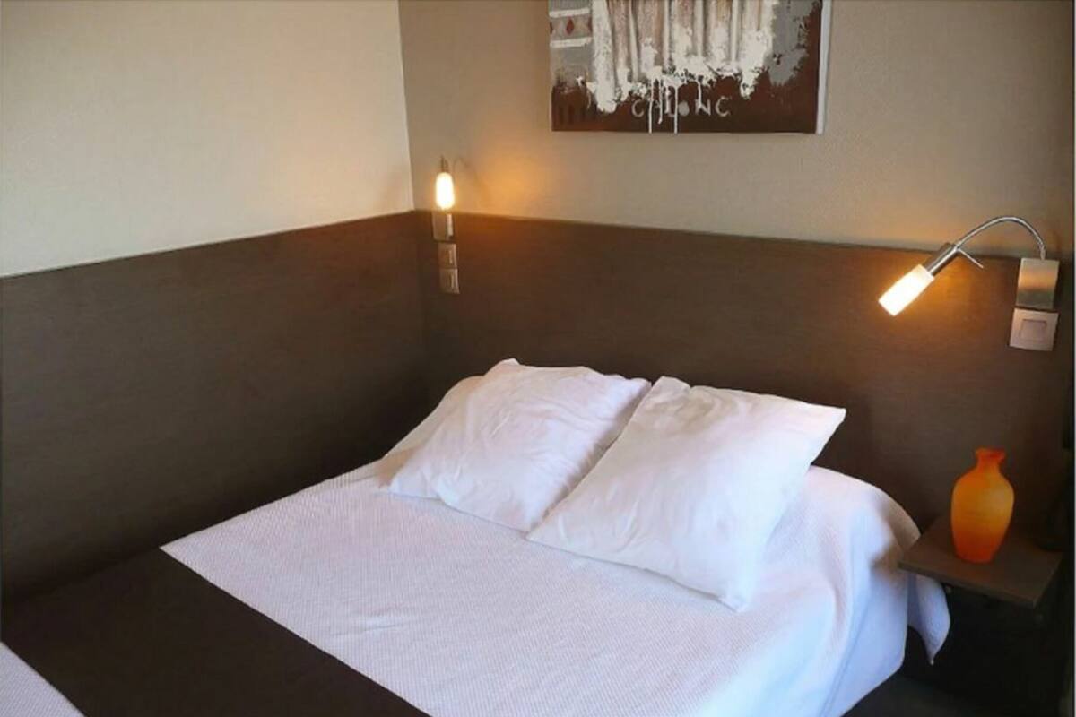 A neatly made bed with white linens and two wall-mounted reading lamps on either side.