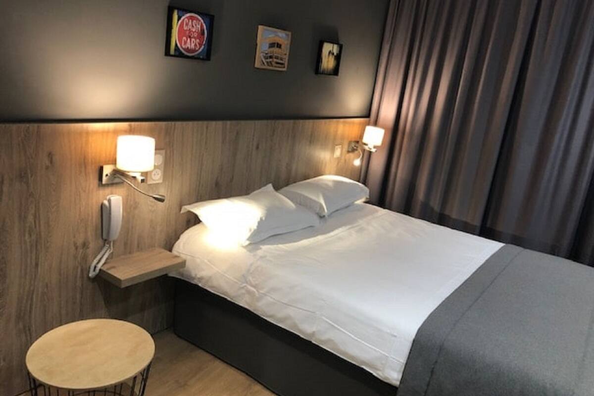 A hotel room with a bed, bedside lamps, a phone, a small table, and wall decorations.