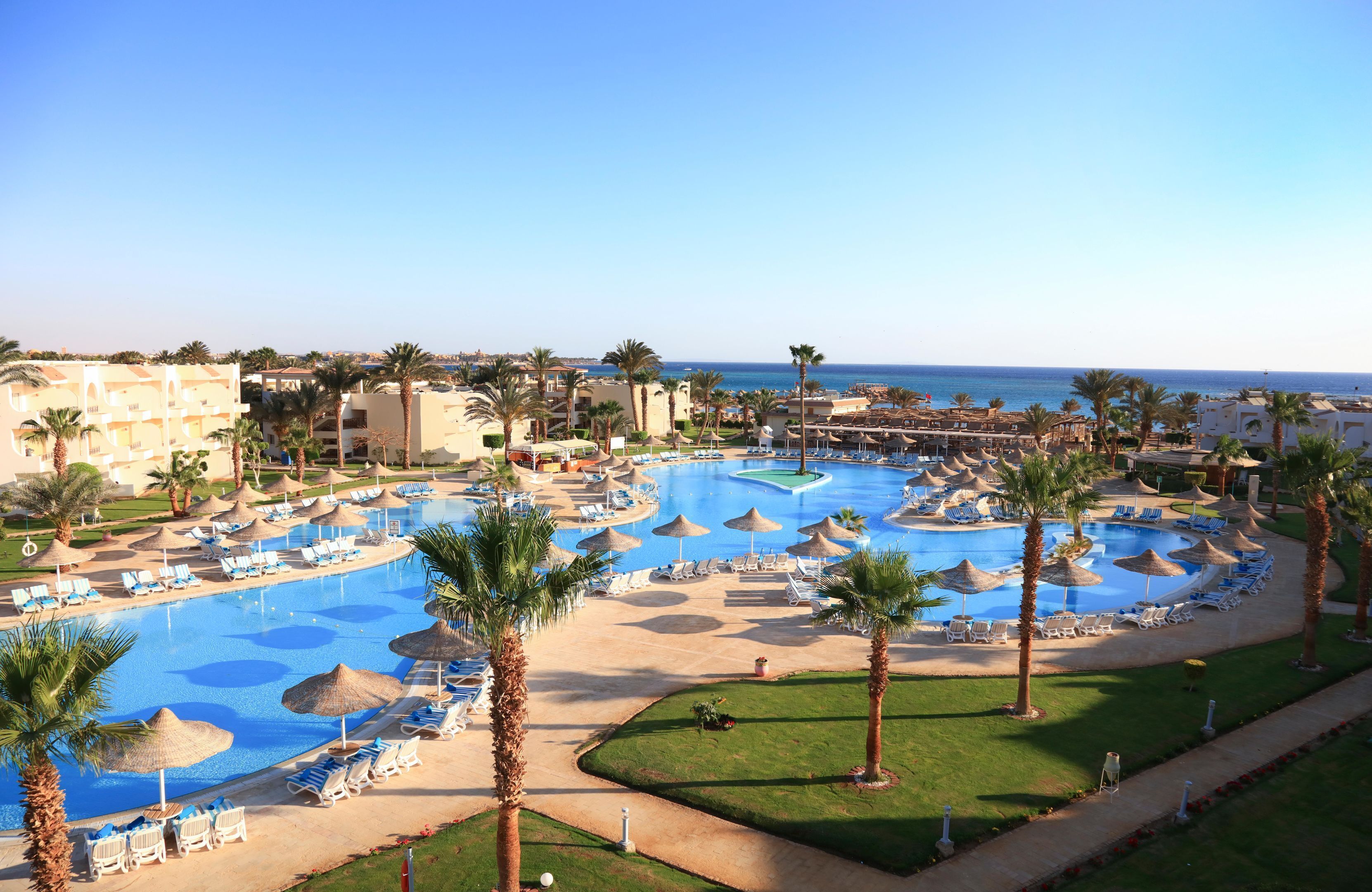 A resort with a large swimming pool, palm trees, and beach umbrellas.