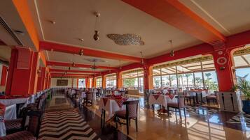 A spacious dining area with multiple tables and chairs, large windows, and a decorative ceiling.