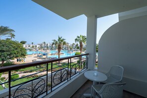 A balcony with a view of a pool area, including lounge chairs and palm trees. - JAZ Palmariva Beach (Makadi Bay)